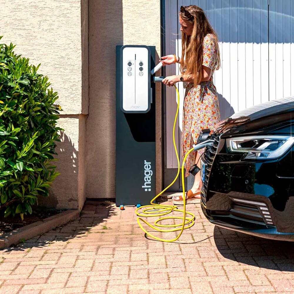Femme qui charge son véhicule grâce à une borne de recharge witty de Hager, devant son garage