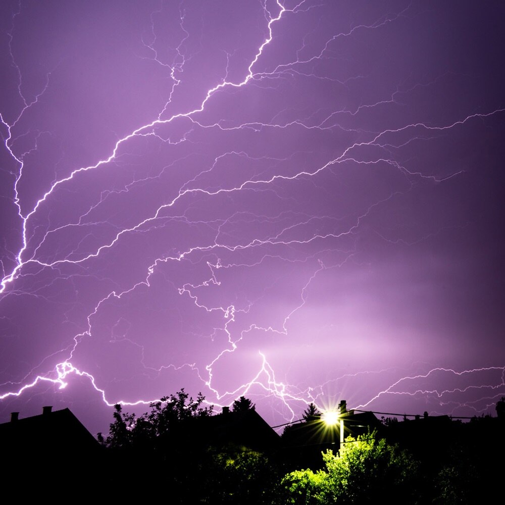 éclairs illuminant le ciel en violet contrastant avec des arbres éclairés par un lampadaire