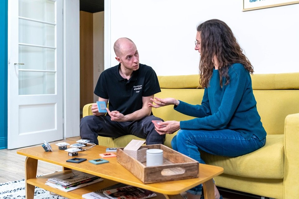 Electricien Elexium de Hager qui présente toute la gamme essensya à une cliente, chez elle