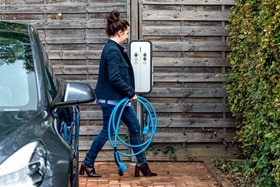 femme tenant un câble de recharge pour charger son véhicule grâce à une borne de recharge witty de Hager dans un parking extérieur