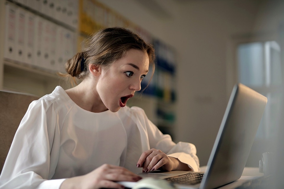 jeune  femme très surprise devant son PC en lisant l'article de blog "5 préjugés sur les véhicules électriques  (qu’il va falloir oublier !)" de Hager