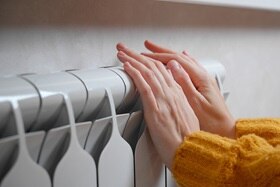 personne qui se réchauffe les mains devant un radiateur électrique