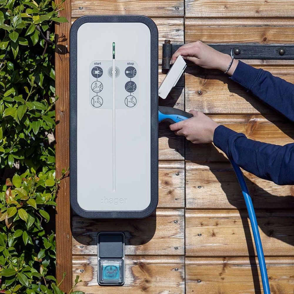 Mains en train de brancher un câble de recharge pour voiture électrique sur une borne de recharge witty solar de Hager