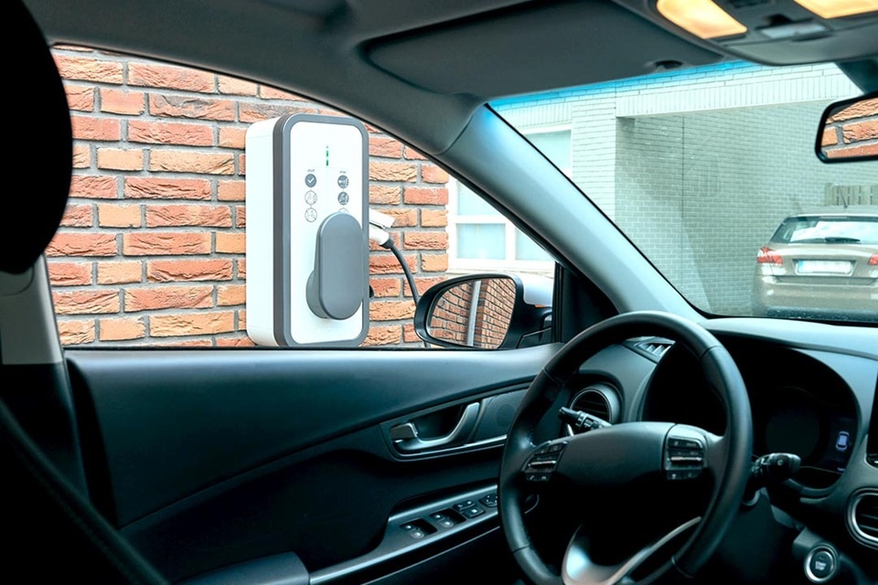Borne de recharge witty start de Hager fixée sur un mur en brique vue de l'intérieur d'un véhicule électrique, fenêtre conducteur ouverte