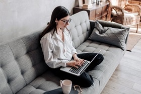femme assise en tailleur sur son canapé avec son PC portable posé sur elle