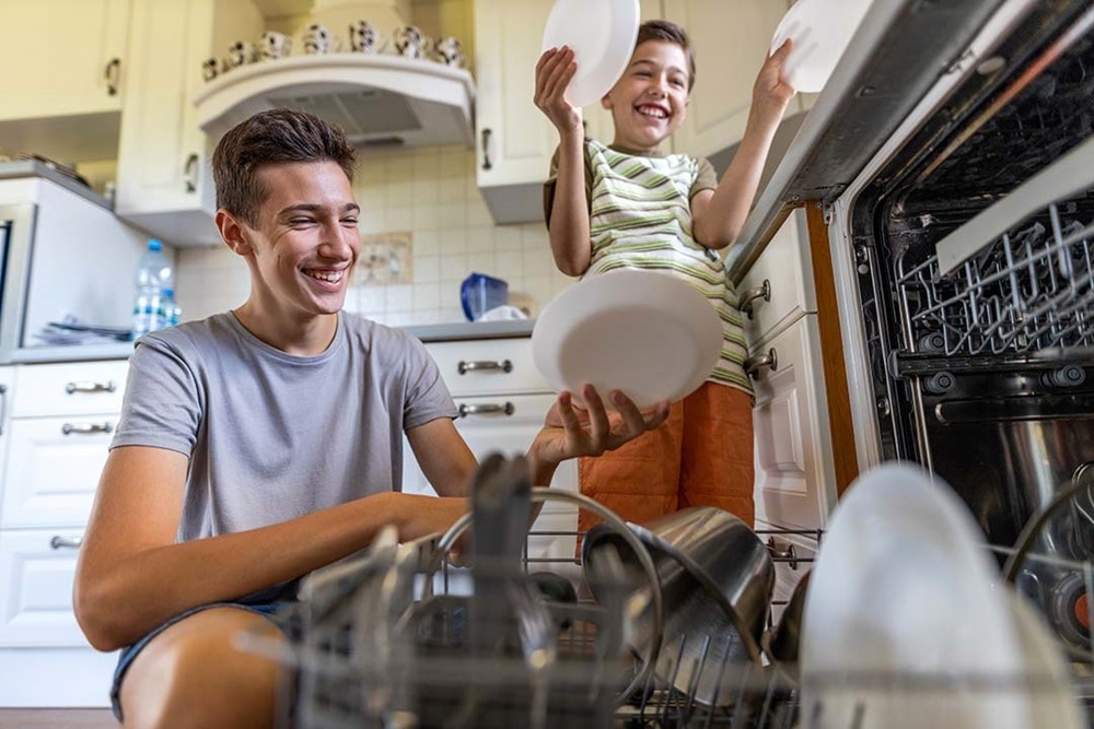 Two boys put dishes in the dishwasher