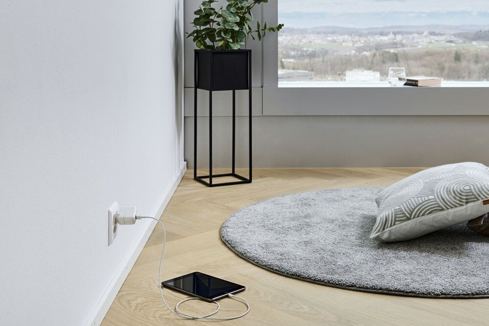 Hager Group Coin salon avec plante et tablette en charge sur une prise électrique