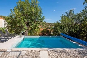 Hager group Piscine extérieure entourée de pierres beiges et d'arbres tout autour