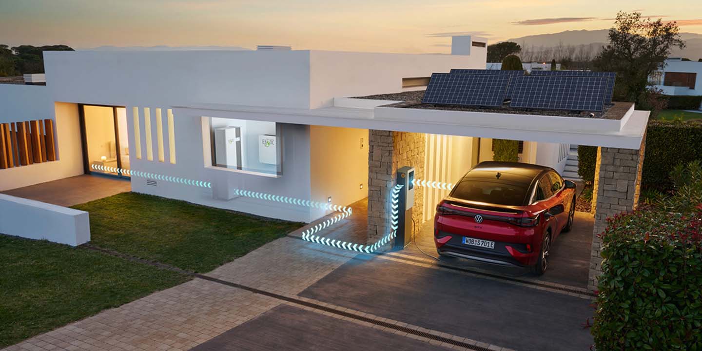 Red electric car in driveway of a modern house with solar panels at dusk.