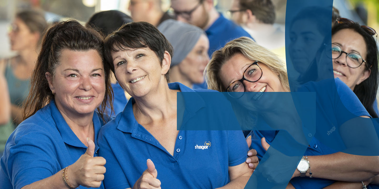 Hager Group employees in blue polo shirts smiling and giving thumbs up at a company event.