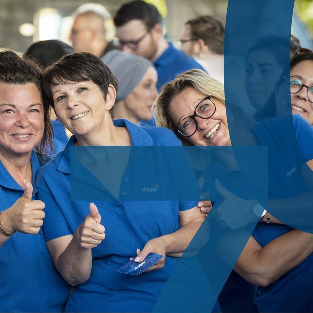 Hager Group employees in blue polo shirts smiling and giving thumbs up at a company event.