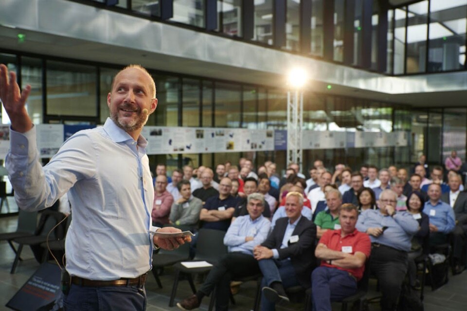 Presenter speaking at a corporate event with audience in background