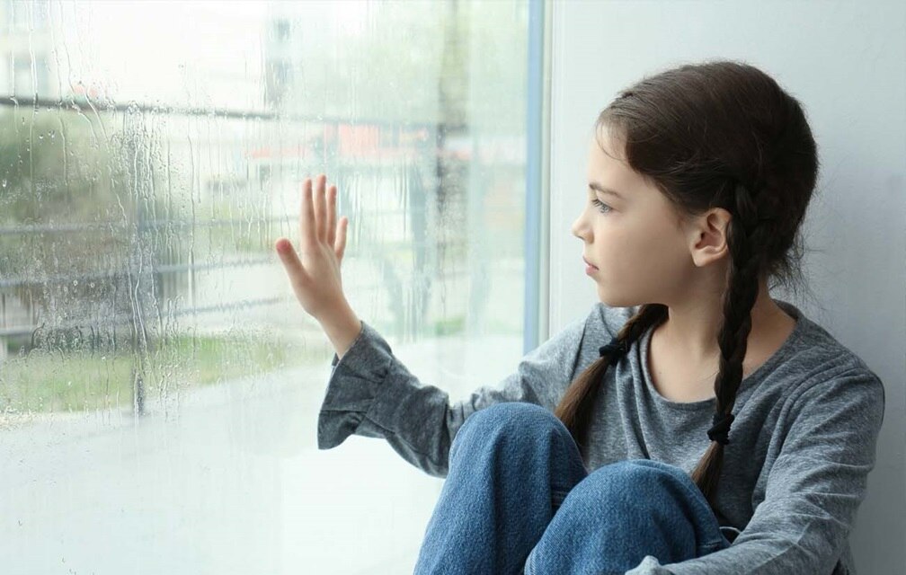 Personne assise à l'intérieur regardant par une fenêtre rayée de pluie