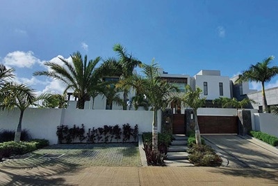 Maison de luxe moderne avec palmiers, clôture et allée sous un ciel bleu