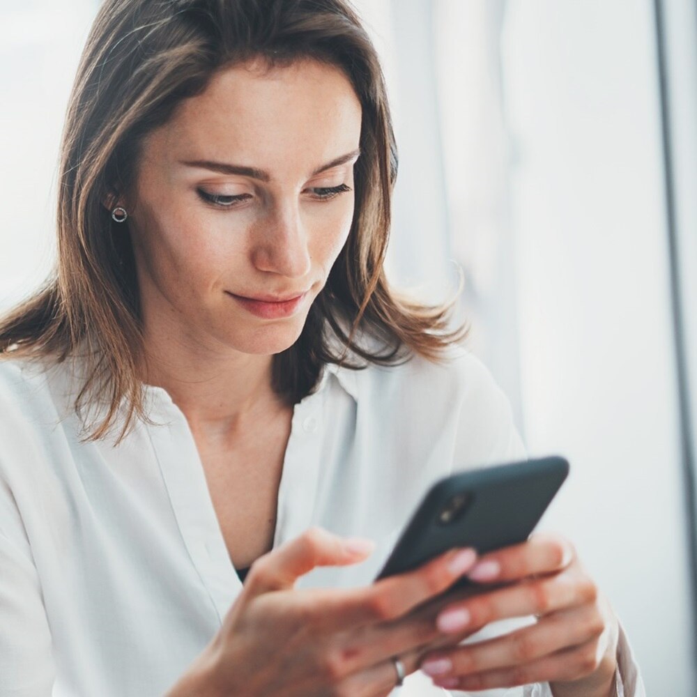 Donna vista frontalmente con uno smartphone in mano che consulta l’app domovea per la smart e building automation