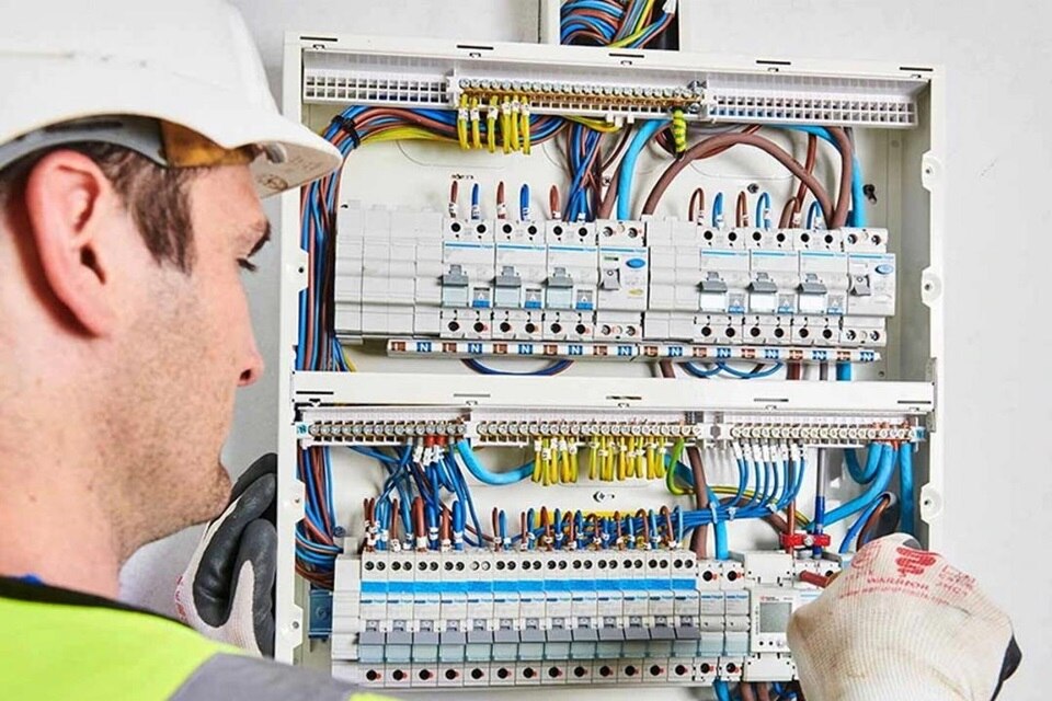 Installatore dotato di dispositivi di protezione con cacciavite in mano di fronte ad un quadro elettrico aperto che verifica l'esatta installazione dei dispositivi di rile­va­zione di guasti d’arco AFDD