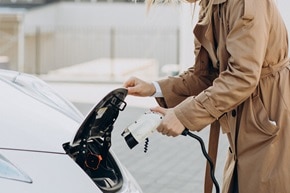 Donna che collega un'auto elettrica alla colonnina di ricarica trifase in un parcheggio urbano