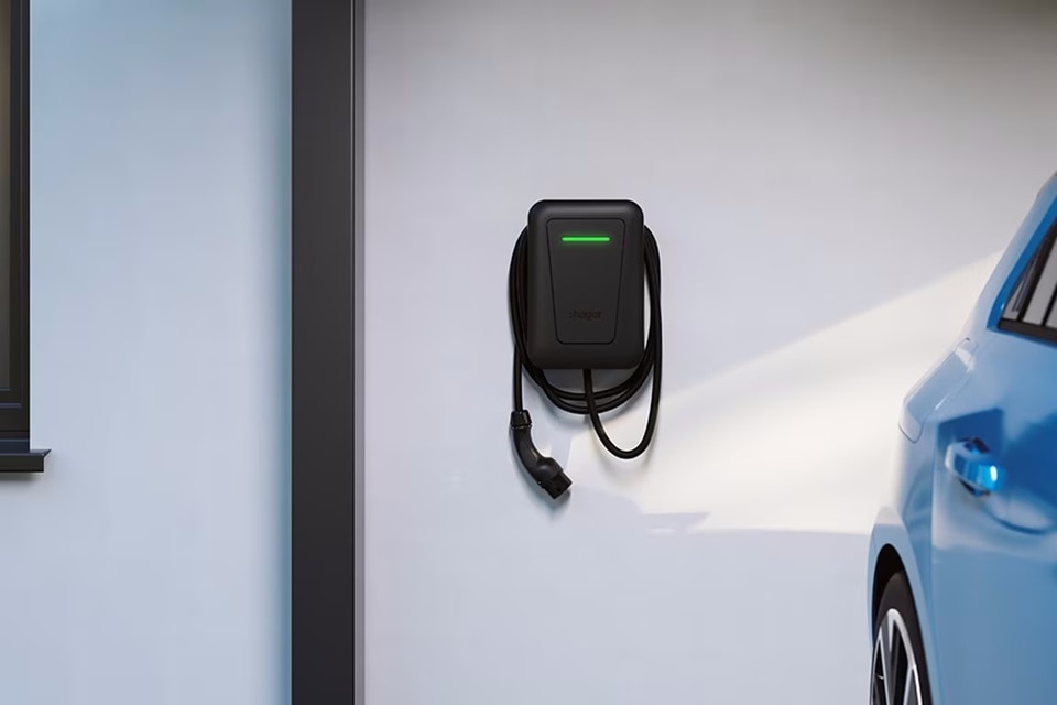 Vista frontale di una colonnina di ricarica witty nera a parete con led verde acceso, a fianco di una vettura vista parzialmente.