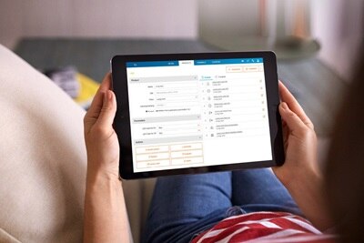 Donna di spalle seduta sul divano con un tablet in mano che consulta l’app domovea per la smart e building automation