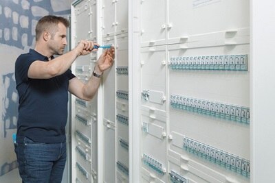 Elettricista che installa e cabla componenti modulari all’interno di un quadro elettrico Hager, utilizzando un cacciavite e maneggiando interruttori automatici per la distribuzione sicura dell’energia.