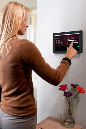 Donna che interagisce con un pannello di controllo domotico a muro domovea di Hager, parte di un sistema di gestione intelligente della casa.