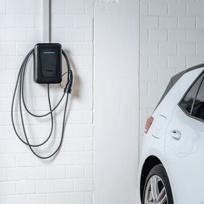 Vista frontale di una colonnina di ricarica witty nera con cavo a parete con led verde acceso, a fianco di una vettura vista parzialmente.