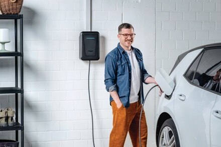 Uomo ricarica l’auto elettrica con colonnina witty one Hager a frontalino nero, montata a parete all’interno di un garage residenziale.