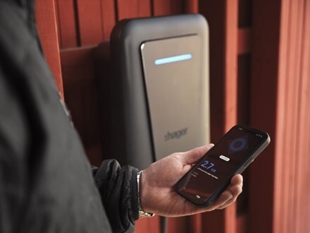 Dettaglio di uomo che utilizza l’app Hager Charge per gestire la ricarica dalla colonnina di ricarica witty one Hager, montata a parete nel garage di casa.