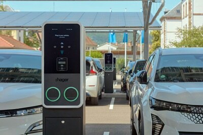 Parcheggio parzialmente coperto per auto elettriche con pannelli solari sul tetto. In primo piano due auto, al centro una colonnina di ricarica witty Park 2 con due punti di ricarica