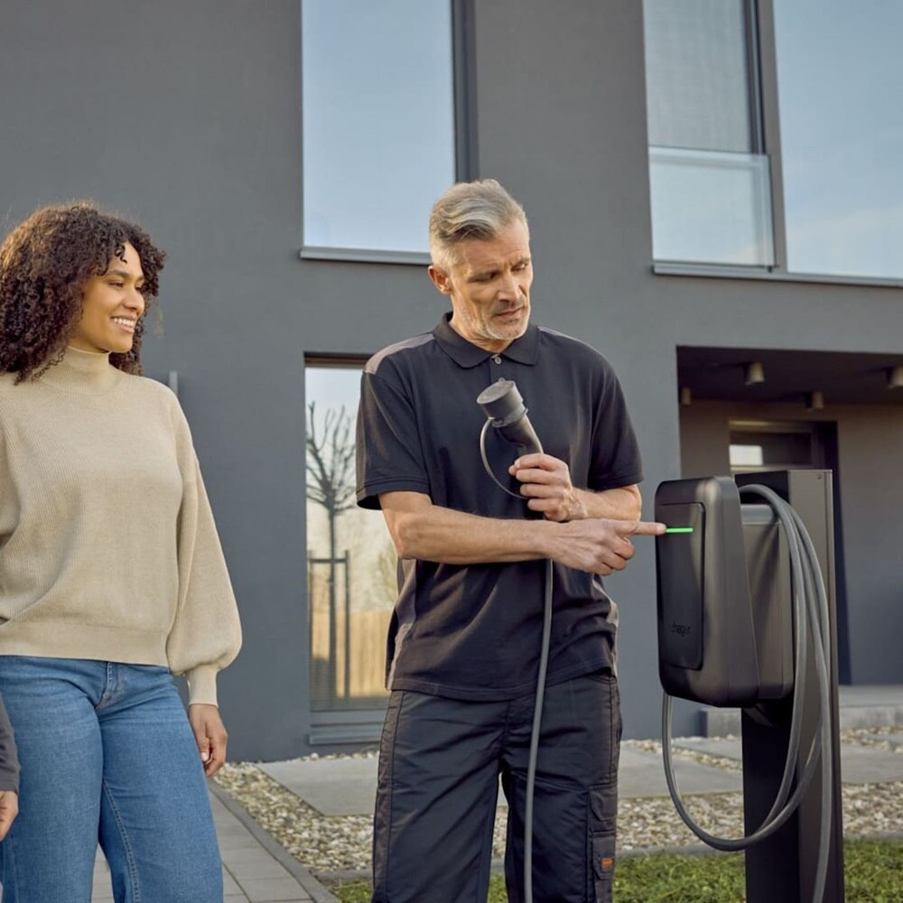 Installatore che mostra alla cliente l’utilizzo della colonnina di ricarica per veicoli elettrici witty plus con cavo, montata su colonna di supporto
