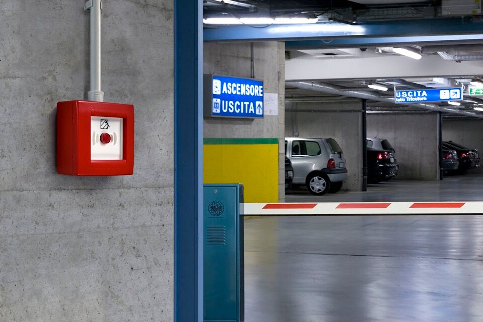 Parcheggio pubblico sotterraneo. In primo piano, montato su una colonna il centralino di emergenza Pablo IP55 CE PULS R con pulsante illuminabile.