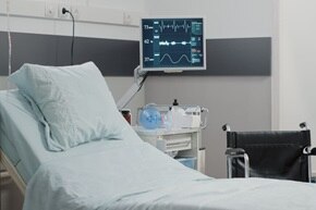 Camera di ospedale con letto dotato di monitor collegato e sedia a rotelle a destra