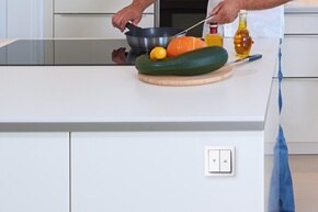 Esempio di installazione dell'interruttore per tapparelle Berker Enocean con bilanciere a 2 vie e simboli freccia per su e giù su isola della cucina. Nello sfondo un uomo sta cucinando su una piastra ad induzione