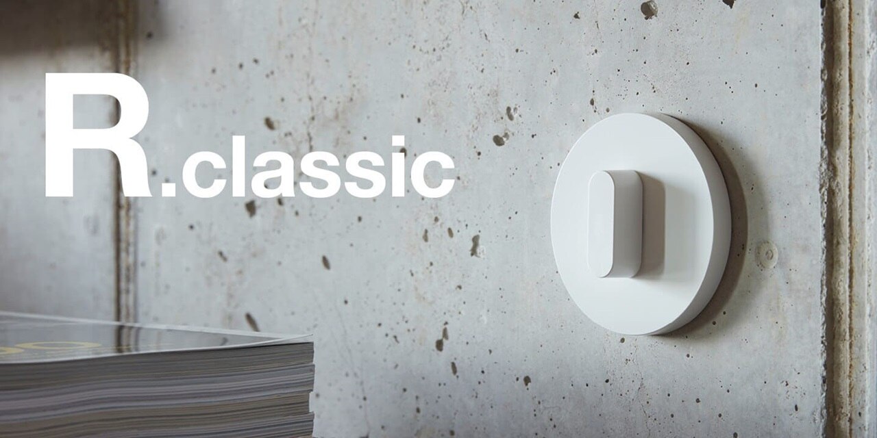 Vista del muro in cemento a vista con interruttore della luce bianco con interruttore rotativo e cornice rotonda bianca della gamma di interruttori Berker R.classic e relativa scritta