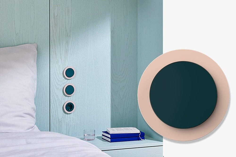 Interruttore Berker R.Classic personalizzato in doppio tono rosa e verde, realizzato su richiesta nella manifattura Berker per un progetto di famosi architetti, installato su pannello in legno chiaro accanto a un letto moderno. In primo piano un interruttore frontale.