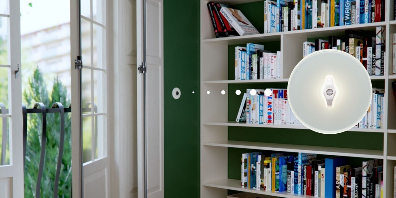 Esempio di installazione interruttore Hager serie Glas bianco con interruttore rotativo nero, su parete verde di uno studio, con libreria e finestra sullo sfondo. Elemento grafico evidenzia l'interruttore frontale
