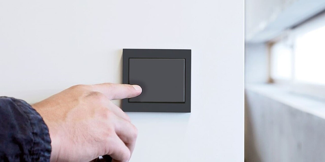Una mano maschile preme l'interruttore Berker K.1 in primo piano, installato su parete bianca