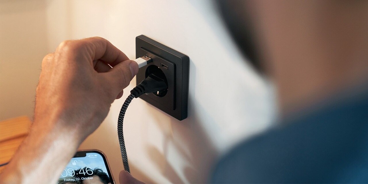 Una persona collega un cavo USB a una presa di corrente a muro dotata di porte USB integrate.