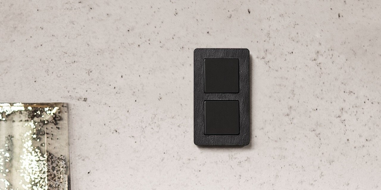 Esempio di installazione di un interruttore della luce Berker Q.7 a 2 moduli con un singolo interruttore a bilanciere nero e una cornice effetto pietra naturale/ardesia su una parete marmorizzata.