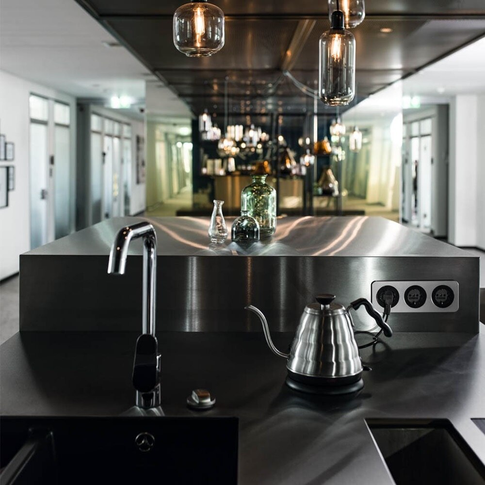 Esempio di installazione di prese Berker R.1 con elemento centrale rotondo in nero e cornice arrotondata in acciaio inox su superficie in acciaio inox zona cucina