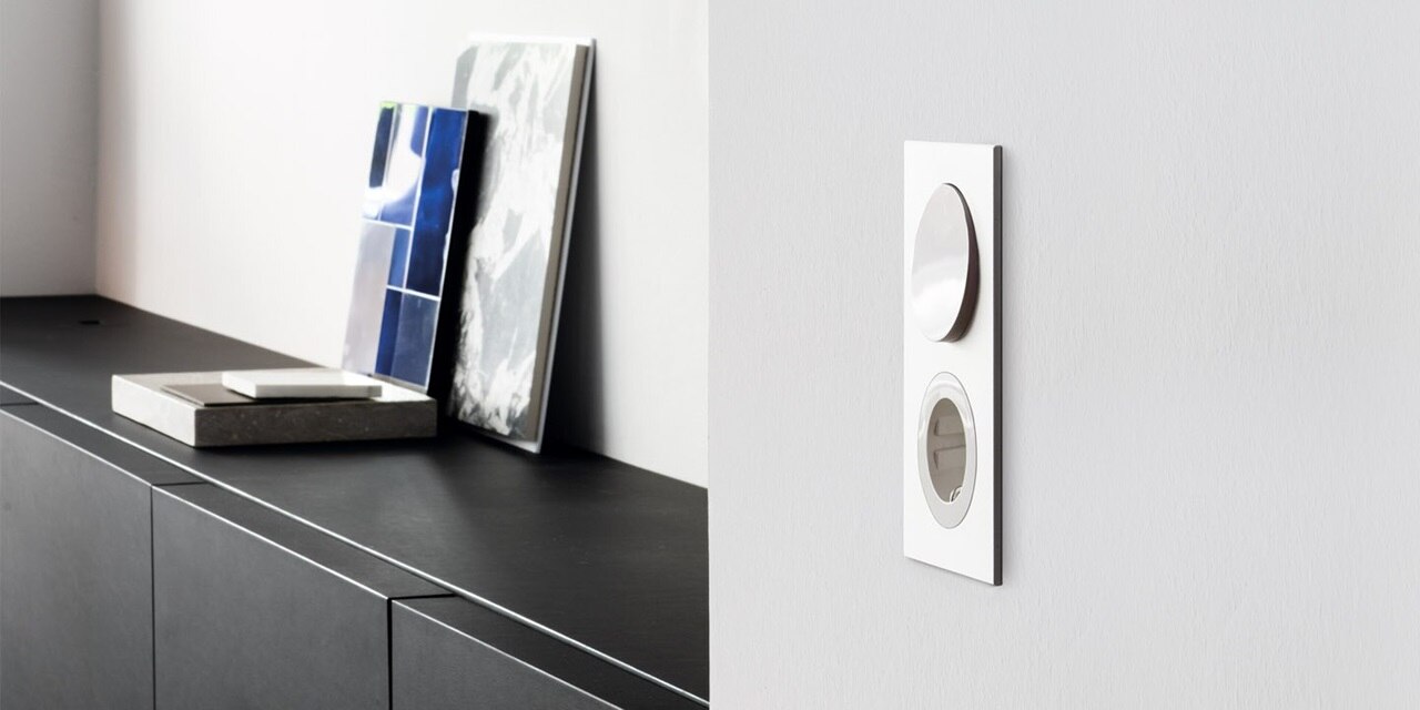 Esempio di installazione dell'interruttore e della presa Berker R.8 con cornice in bianco lucido in design piatto su una parete grigio chiaro di uno negozio espositivo