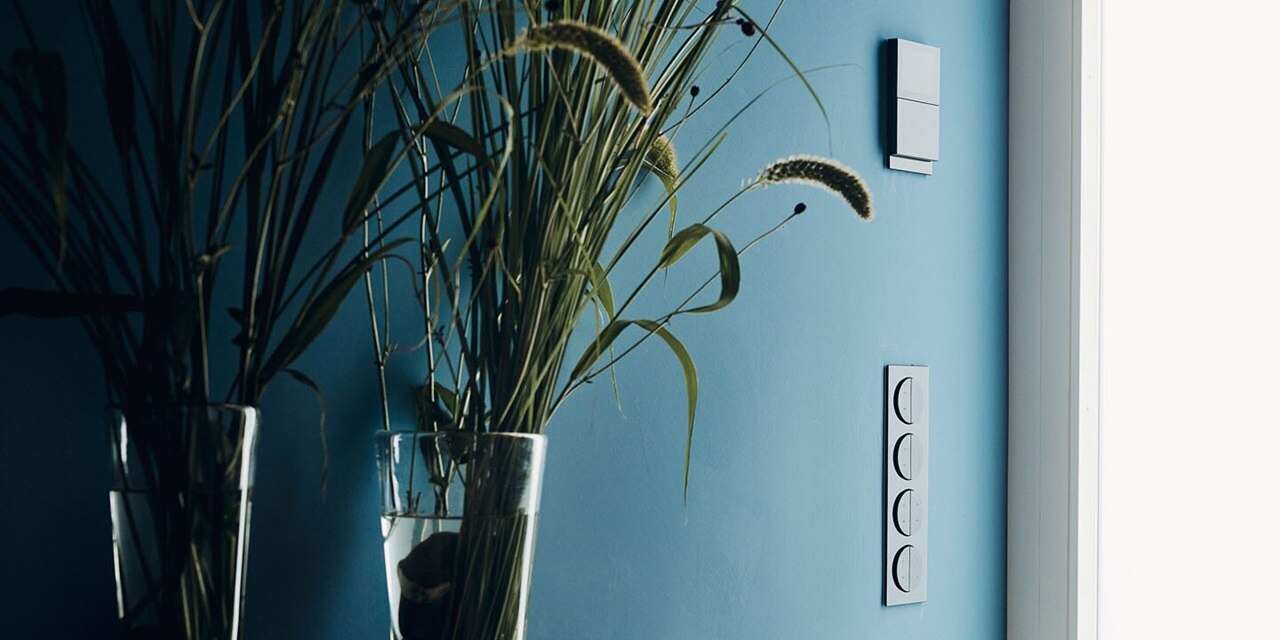 Esempio di installazione verticale del pulsante Berker R.8 a 2 vie con elemento centrale rotondo e cornice a 4 moduli in nero lucido su una parete blu di un ingresso