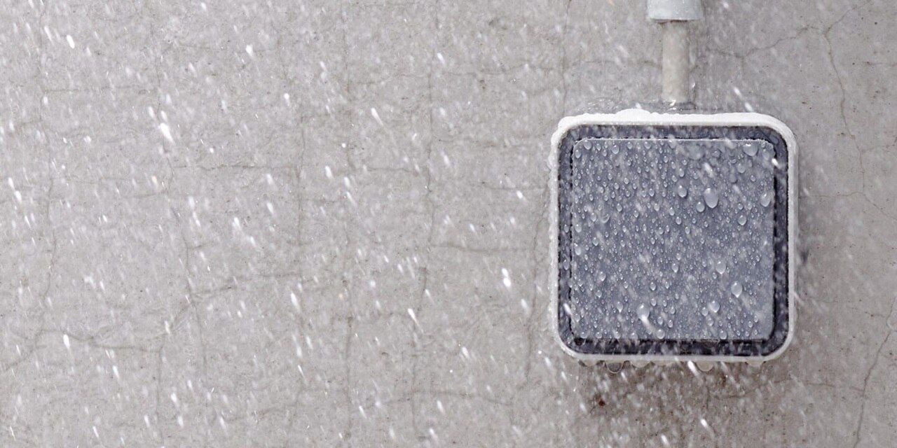 Esempio di installazione dell'interruttore della luce Berker W.1 AP con bilanciere grigio su un muro di cemento sotto la pioggia, vista frontale