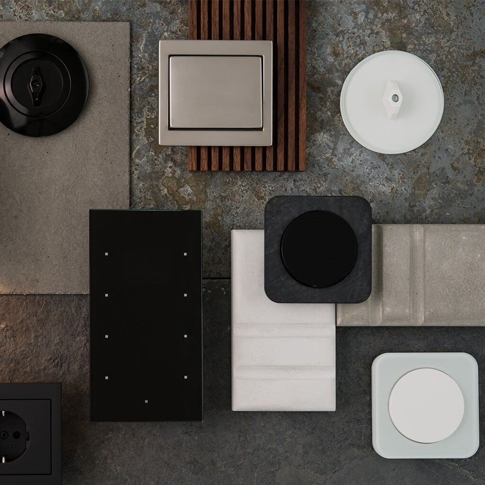 Panoramica di una serie di interruttori Berker di forme e colori diversi esposti su una piastrella di ceramica insieme a campioni di materiali