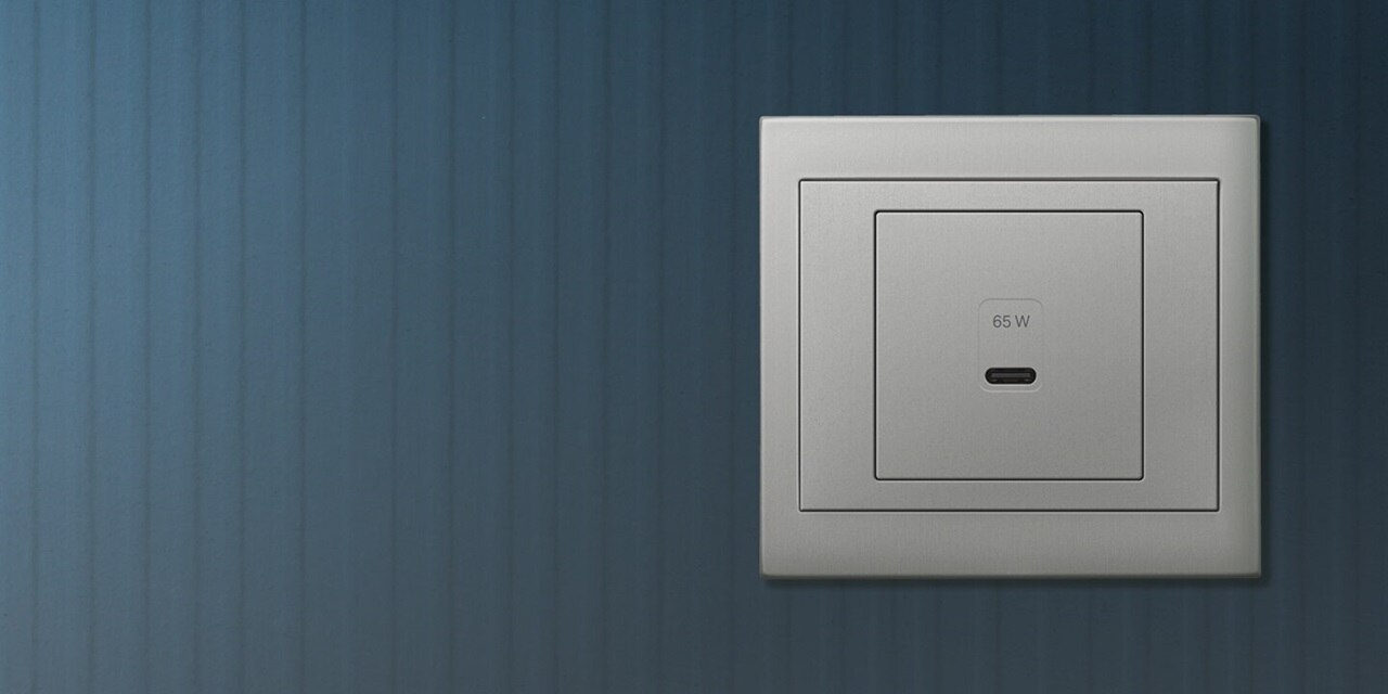 Vista frontale della presa di ricarica USB Berker K.5 da 65 watt con una porta di ricarica USB-C e telaio in alluminio su sfondo blu