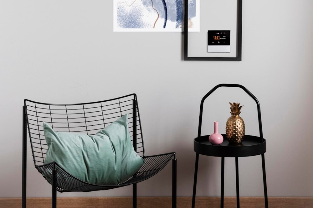 Interno di design con poltroncina e tavolino di fronte a parete con diverse cornici al cui interno è presente il cronotermostato KNX Berker
