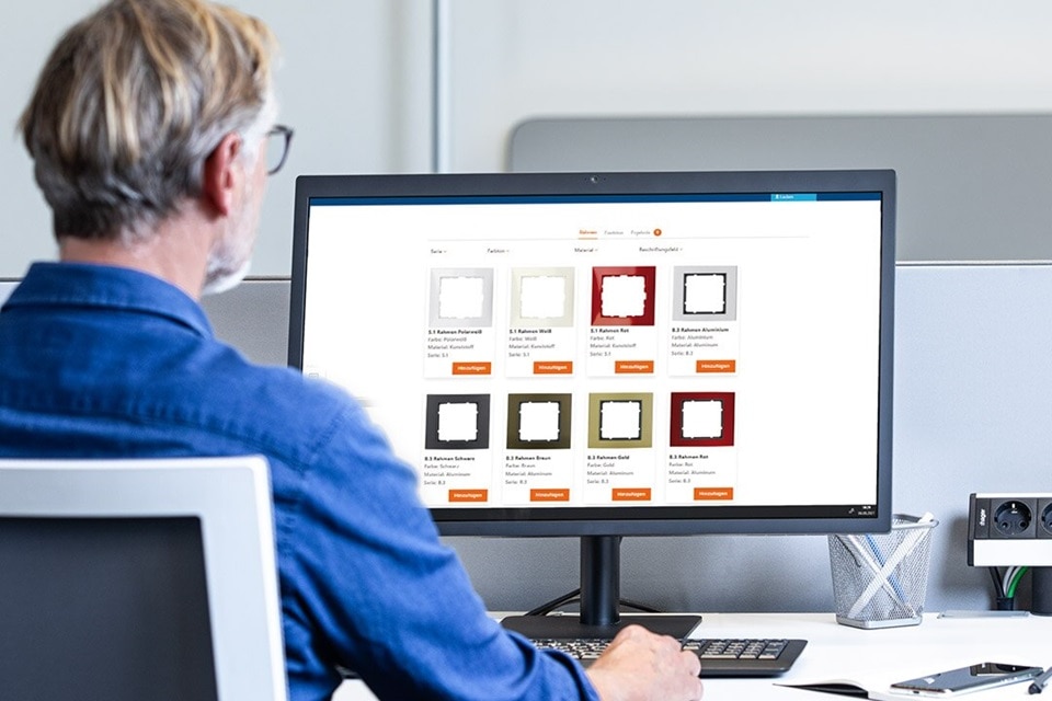 Immagine di un elettricista di spalle che utilizza il configuratore di interruttori e prese Berker sul monitor del PC posizionato sulla scrivania