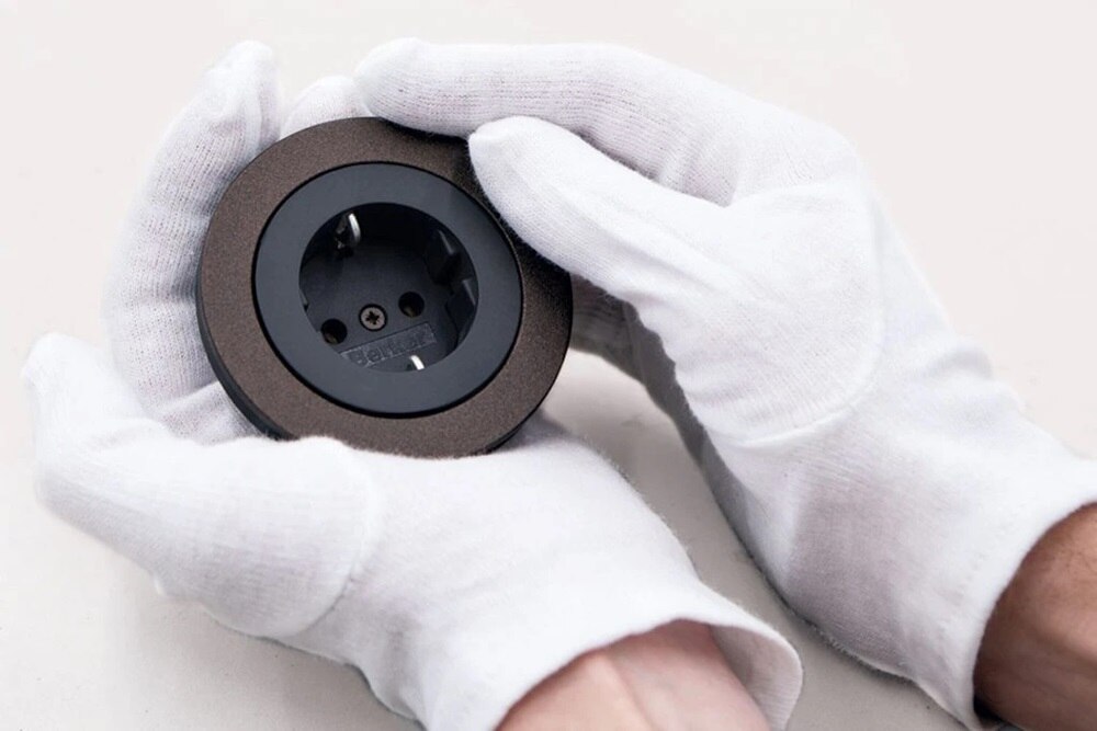 Due mani avvolte in guanti bianchi tengono stretta una presa rotonda con materiali personalizzati, grazie alla manifattura Berker 