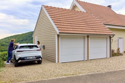 Coppia ricarica l’auto elettrica con la colonnina di ricarica witty one Hager montata a parete sul muro esterno di casa.