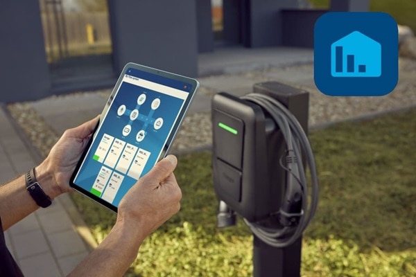 Wallbox witty plus nella versione con cavo installata su colonnina di fissaggio per parcheggi privati o aziendali. In primo piano in mano tablet con l’app hager flow per la gestione dei flussi dell’energia generata dal sistema fotovoltaico